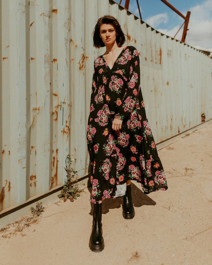Marine Debut portant une longue robe noire fleurie devant un décor industriel